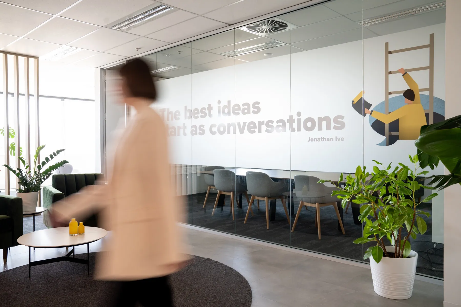 Inside the Brighter studio, with glass meeting rooms, plants and a person walking through the space